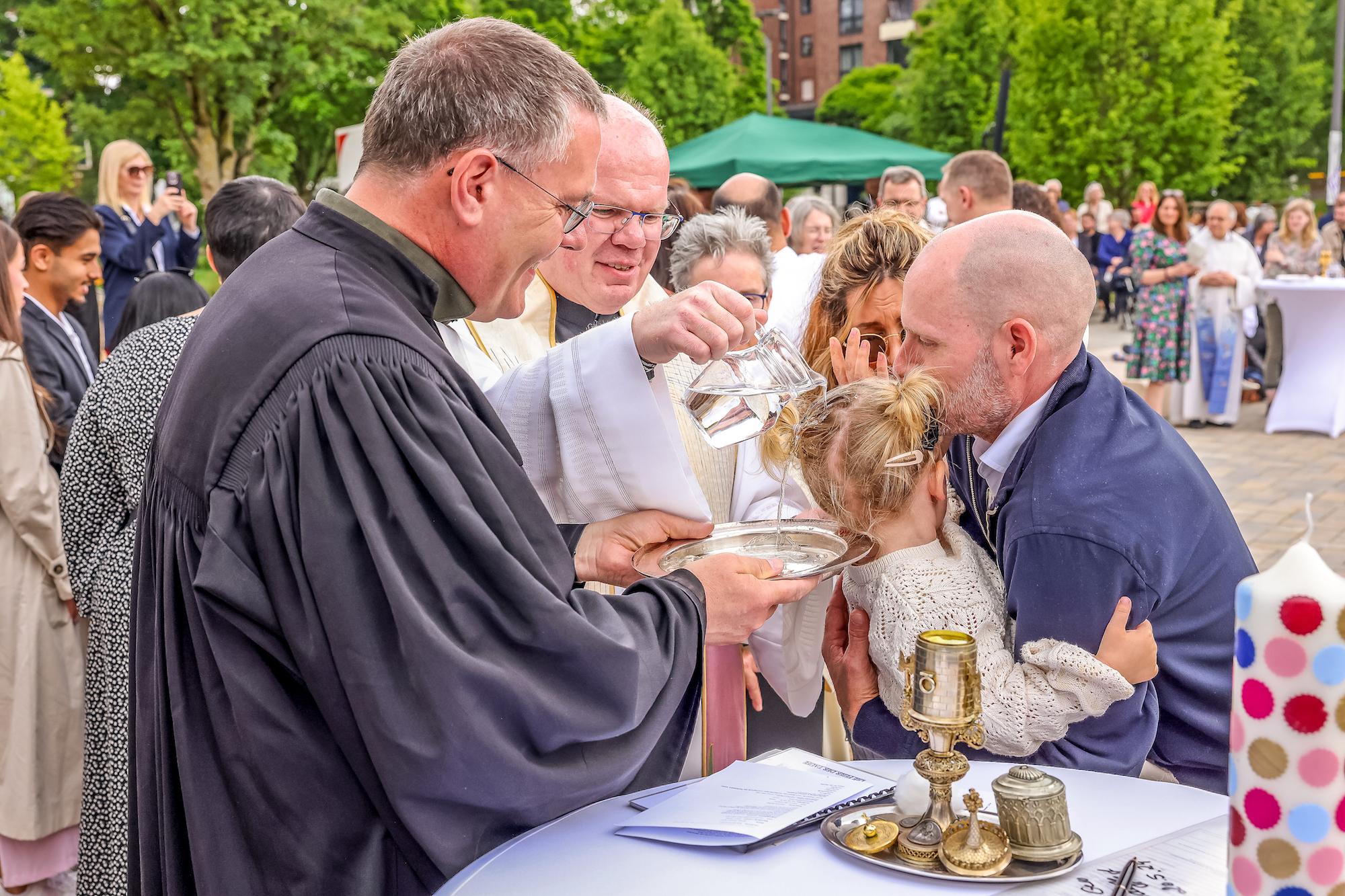 Während Regionalvikar Ulrich Clancett das Sakrament spendet, hält sein evangelischer Kollege Till Hüttenberger die Taufschale.